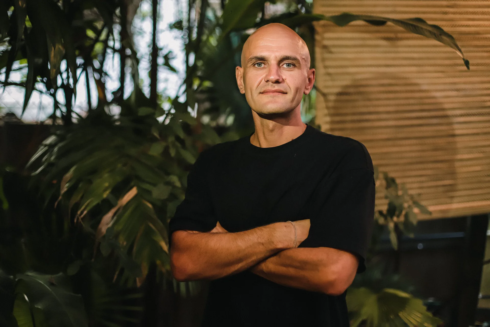 GANGSTANTIN standing with folded arms among tropical plants.