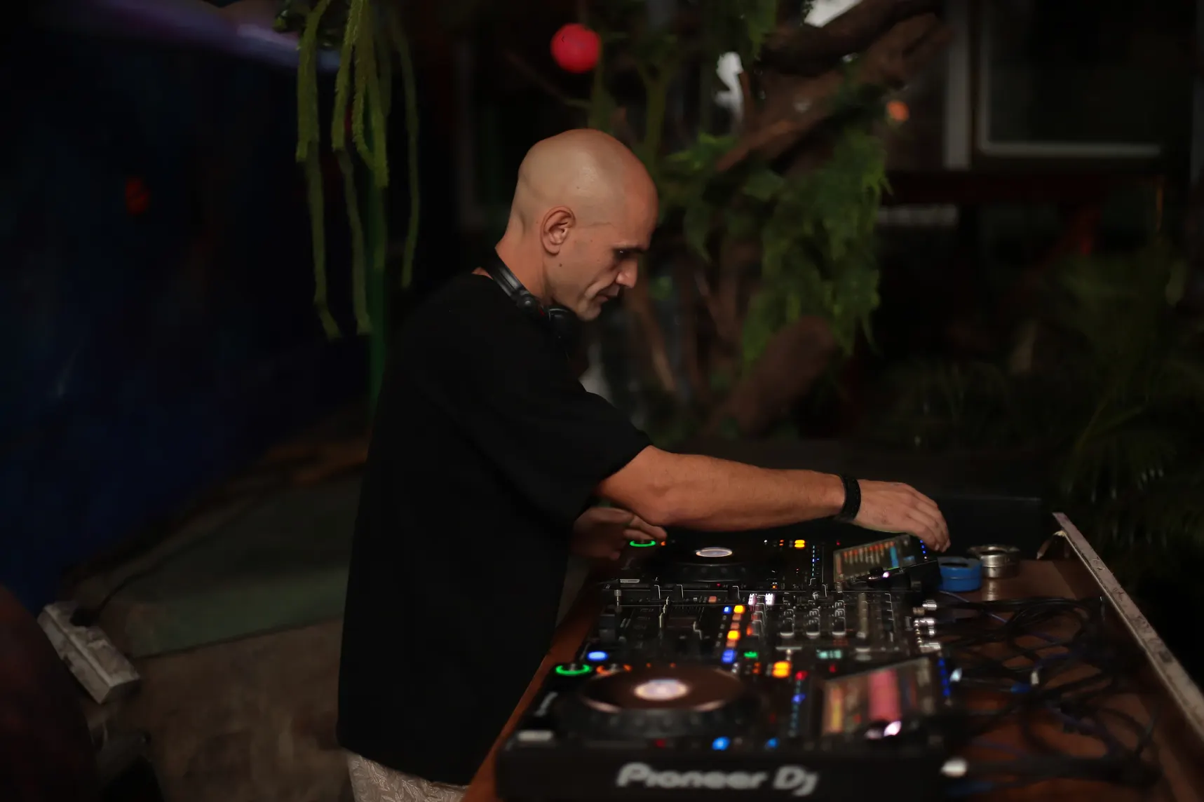 GANGSTANTIN performing at a DJ setup surrounded by plants.