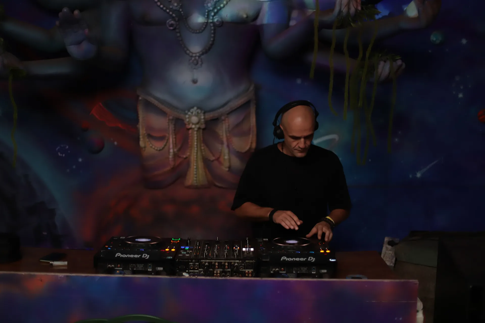 GANGSTANTIN performing at a DJ booth in front of a painted mural.