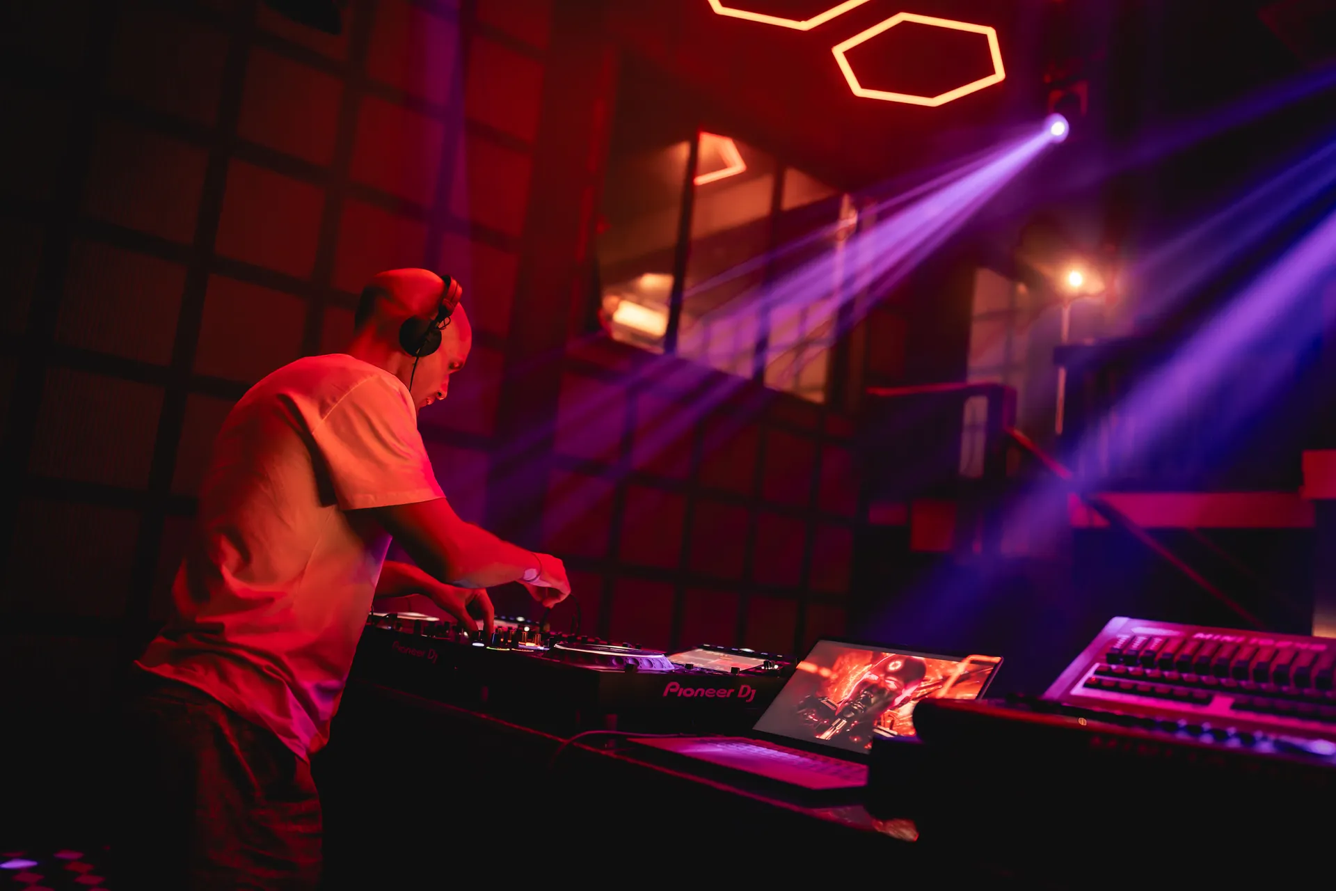 GANGSTANTIN performing at a DJ booth under red and violet stage lights.