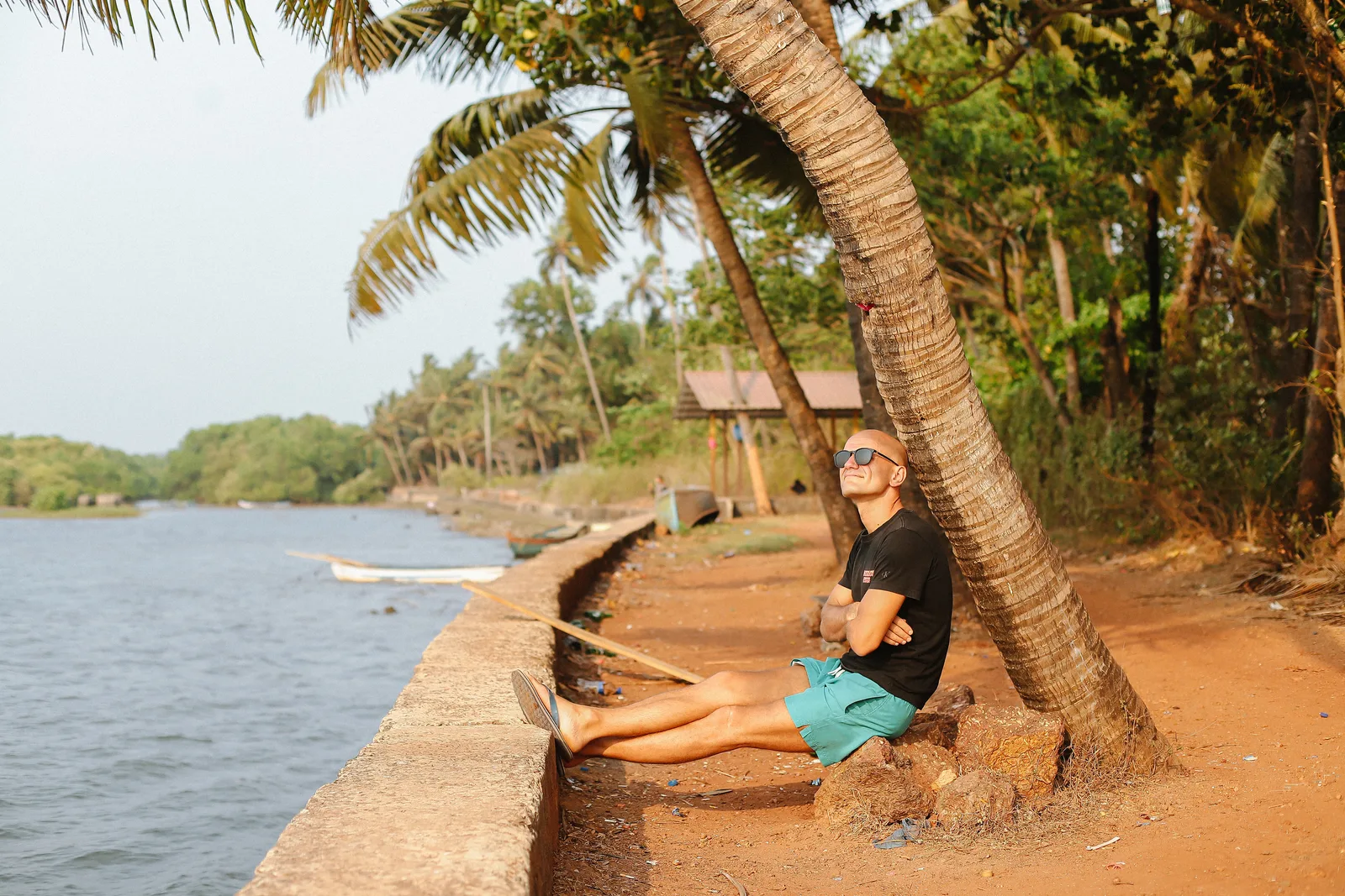 GANGSTANTIN seated beneath a palm tree beside the water.